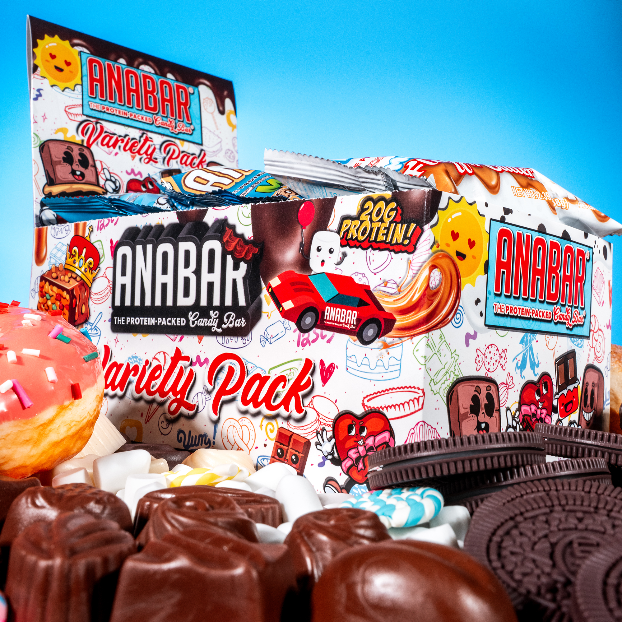 The Anabar Variety Pack - 12 Bars by The Anabar features a vibrant box labeled “Variety Pack,” surrounded by delicious flavors like assorted chocolates, cookies, and frosted donut, with playful cartoon graphics on a bright blue background.