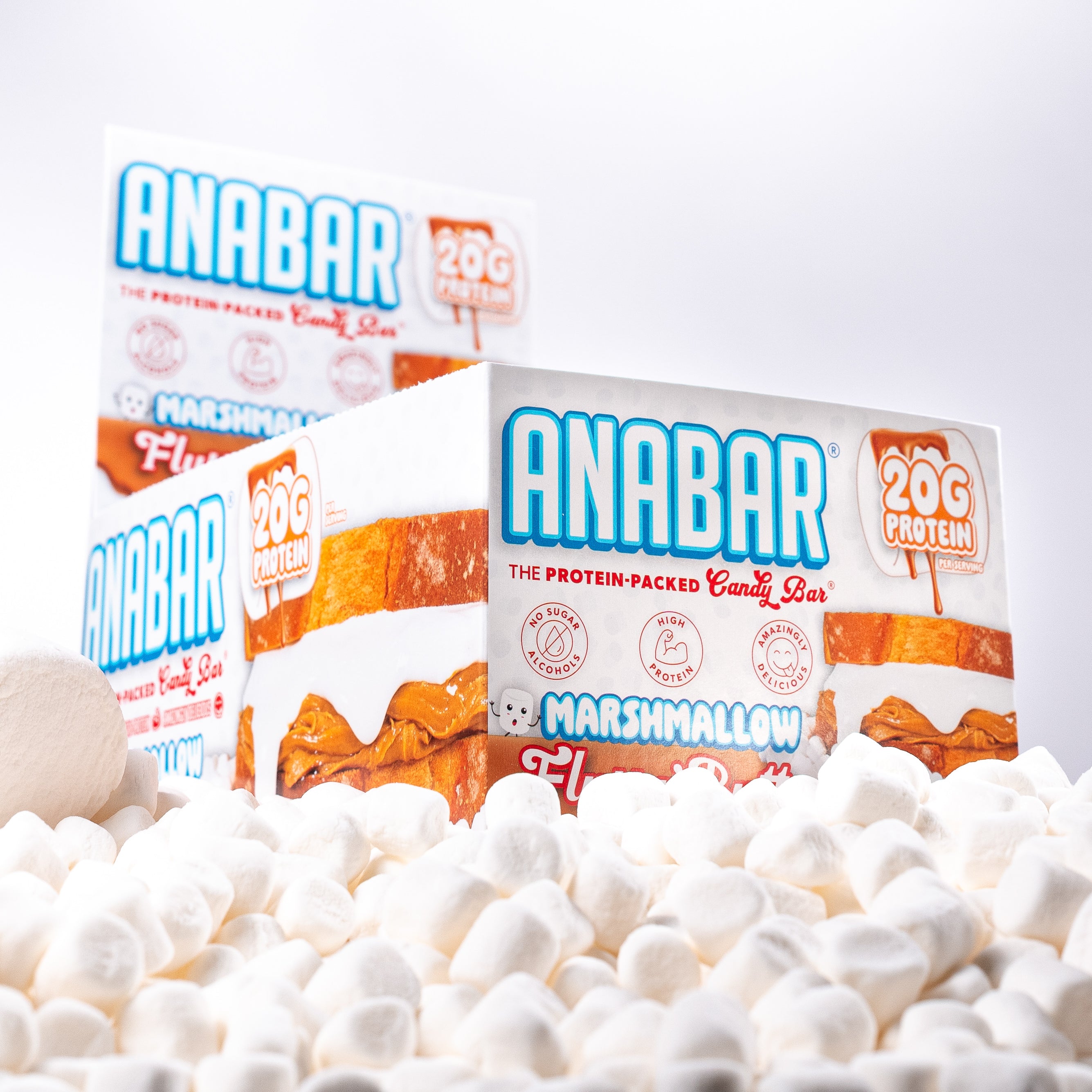 A box of The Anabar Fluff n' Butter protein bars sits among mini marshmallows. The packaging features 20g protein per bar, highlights peanut butter and marshmallow flavors, and displays images of the candy bar on the front.