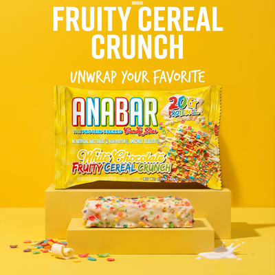 A The Anabar Fruity Cereal Crunch protein bar topped with colorful cereal pieces sits on a yellow pedestal, with its yellow product packaging displayed behind it.