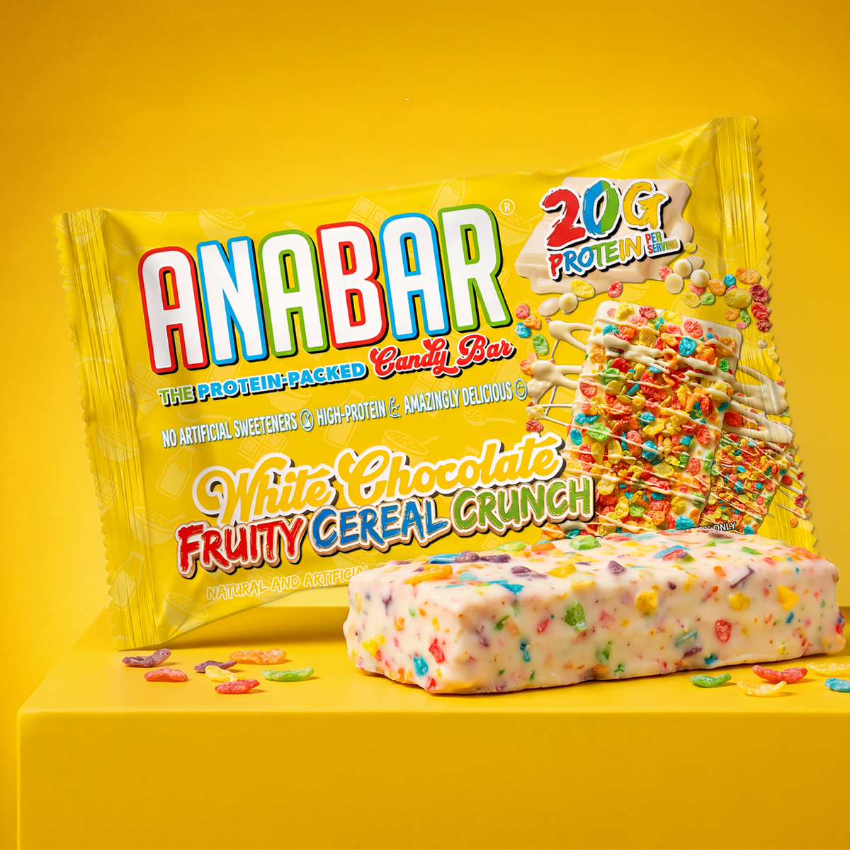 A rectangular The Anabar Fruity Cereal Crunch protein bar topped with colorful cereal pieces, shown in front of its bright yellow wrapper containing 20g protein.