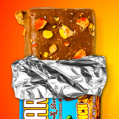 A partially unwrapped Monster Cookie Crunch milk chocolate bar by The Anabar features colorful candy pieces on top, set against a vibrant orange and yellow background.