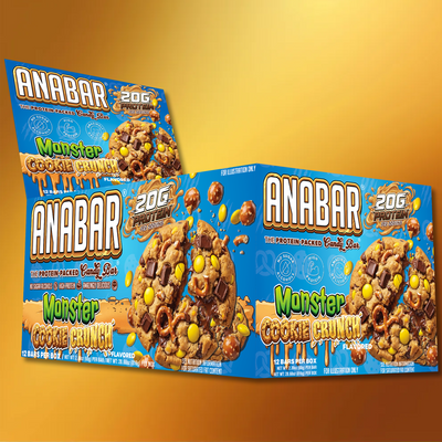 Boxes of The Anabar Monster Cookie Crunch protein bars are displayed on a gold gradient background. The blue packaging features milk chocolate bars filled with colorful candy-coated chocolates and crunchy cookie pieces.