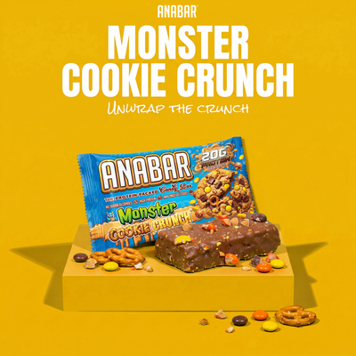 A The Anabar Monster Cookie Crunch protein bar topped with colorful candy pieces and pretzels, positioned in front of its product wrapper.