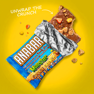 A partially unwrapped Monster Cookie Crunch protein bar with cookie and candy toppings and a bite taken out of one end, set against a yellow background.