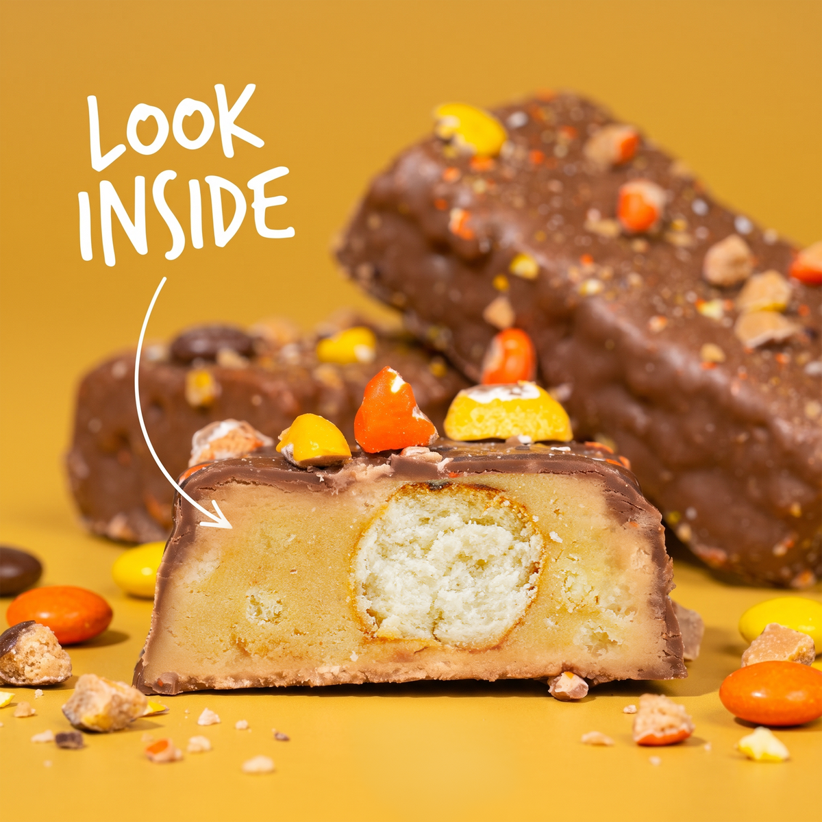 A cross-section of a Monster Cookie Crunch protein bar with a textured center, featuring an arrow pointing to the interior with the text “Look inside.”