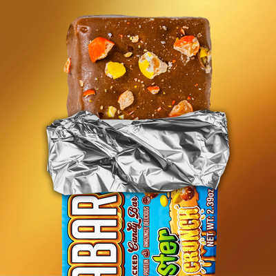 The Anabar Monster Cookie Crunch is a milk chocolate protein bar with colorful candy pieces, partially unwrapped from silver foil and a blue wrapper, set against a golden-yellow background—ideal for Monster Cookie Crunch fans.